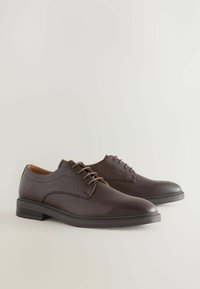 Brown leather dress shoes with a textured surface, lace-up design, rounded toe, and a low heel. Features a contrasting stitched accent.