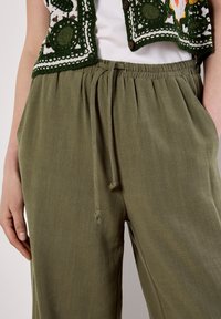 Pantaloni in tessuto verde intrecciato con vita elastica, dettaglio con cordoncino e tasche laterali, caratterizzati da un leggero motivo testurizzato.