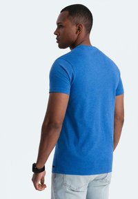 Modrá tričko s krátkým rukávem vyrobené z měkké, texturované látky. Má kulatý límec a rovný lem, ve spojení se světle modrými džíny.