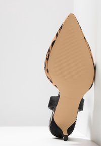 Chaussure à bout pointu pour femme avec dessus imprimé léopard, bride noire et petit talon kitten noir, vue du côté de la semelle sur surface blanche.