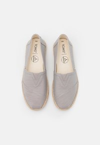 Baskets en toile grises à enfiler avec des accents cousus, semelle en jute de style espadrille et tige en tissu doux. Logo TOMS visible sur la semelle intérieure.