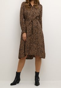 Brun klänning med svart leopardmönster, långa ärmar, krage och bälte i midjan. Bärs med svarta ankelstövlar, fållen är längre bak.