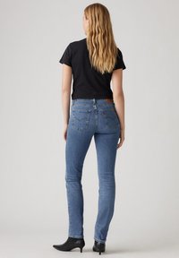 Jean skinny bleu en denim, avec une taille mi-haute, une étiquette logo à l'arrière et des poches arrière classiques. Associé à un t-shirt noir et des bottes.