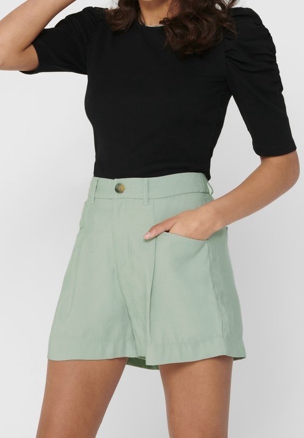 Černý top s nabíranými rukávy spárovaný s vysokými světle zelenými šortkami s bočními kapsami a předním zapínáním na knoflík.