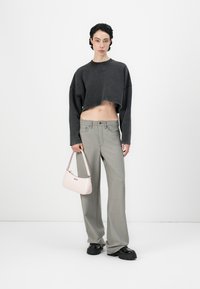 Sweatshirt grigio corto, pantaloni larghi grigio chiaro, scarpe platform nere e una borsa rosa con un logo discreto. Design e texture minimalisti.