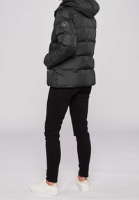 Czarna pikowana kurtka z kapturem, o gładkiej, błyszczącej powierzchni i poziomym przeszyciu; zestawiona z czarnymi, dopasowanymi spodniami oraz białymi trampkami.