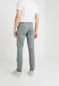 Pantaloni di cotone verde chiaro a taglio slim, dotati di tasche laterali e posteriori, indossati con una maglietta texturizzata beige chiaro e sneakers grigie.