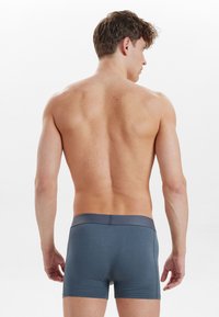 Gray boxer shorts made of soft fabric, featuring a contrasting dark waistband and a snug fit, shown from the back on a model.