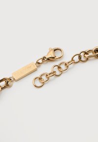 Χρυσό βραχιόλι αλυσίδας με ρυθμιζόμενους κρίκους και κούμπωμα τύπου αστακού, με ορθογώνια ταμπέλα χαραγμένη με τη λέξη "LACOSTE".