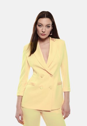 Blazer giallo doppiopetto con scollatura a V profonda, maniche lunghe e due tasche frontali. Texture liscia e design aderente.