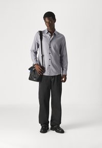 Grijze button-up shirt, zwarte crossbody tas, losse zwarte jeans en zwarte schoenen. Soepele shirtstof, rechte pijpuitvoering, minimale hardwaredetails.