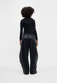 Fekete sportos kapucnis pulóver testhezálló szabással és kapucnival, laza fekete nadrággal, fehér szegélyezéssel és "NIKE" felirattal.