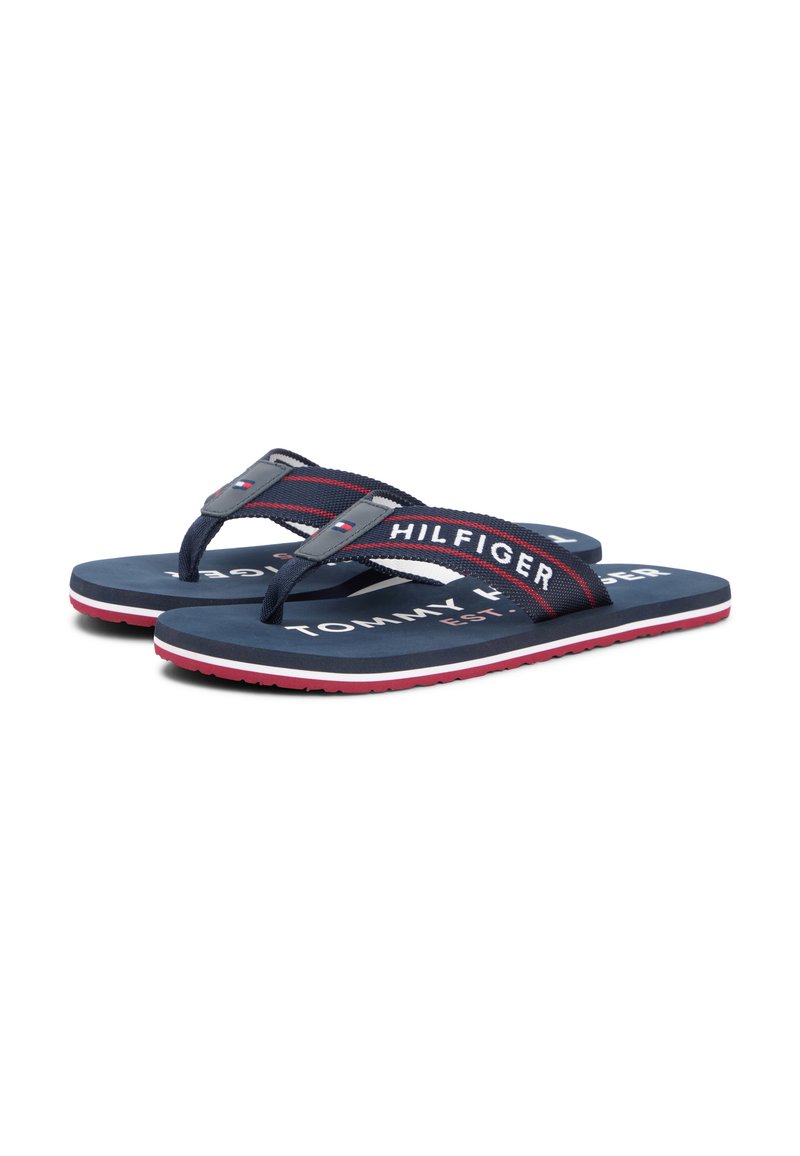 Par de chanclas Tommy Hilfiger azul marino con tiras a rayas rojas y blancas y nombre de la marca en blanco en la plantilla y las tiras.