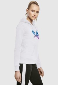 Vit hoodie med en fjärilsdesign i blått och lila, med en framficka och justerbar huva. Visas med svarta byxor.