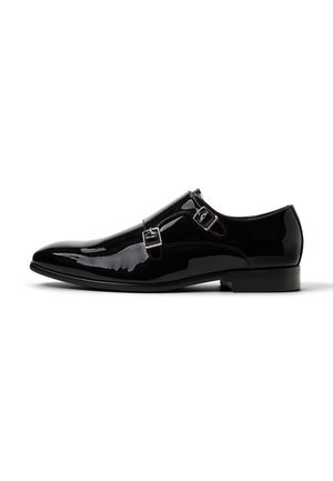 Sort herresko i laklæder med dobbelt monk-strap spænder og lav hæl, vist i profil mod hvid baggrund.