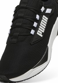 Baskets de sport noires en tissu en maille avec des lacets noirs et blancs. Présente un logo Puma blanc bien en évidence sur un panneau noir. Semelle en caoutchouc, design épuré.