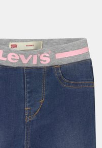 Slim fit jeans i mörkblå denim med orange sömmar, featuring ett grått elastiskt midjeband med rosa "Levi's"-logotyp. Inkluderar en liten framficka.