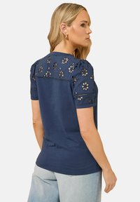 Top azul marino con detalles de ojal floral en las mangas abullonadas y en la parte de atrás, hecho de una tela suave, con escote redondo y dobladillo recto.