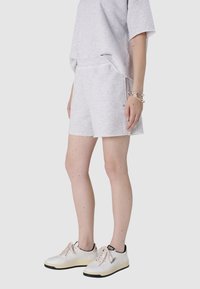 Jasnoszary bawełniany sweter w połączeniu z pasującymi szortami. Szorty mają postrzępiony brzeg, luźny krój i są noszone z białymi i czarnymi sneakerami.