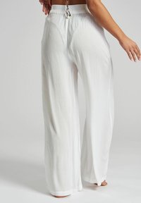 Białe spodnie o szerokich nogawkach wykonane z lekkiego materiału o marszczonej teksturze, z elastycznym pasem i sznurkiem do regulacji z tyłu.