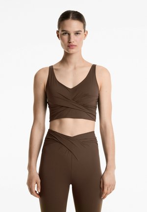 Brun kortärmad träningströja med breda band och V-ringning, med en vriden design fram; ihop med matchande högmidjade leggings.