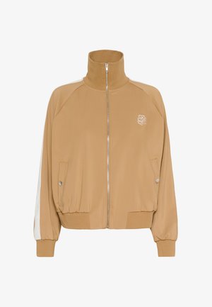 Veste zippée beige avec col montant, poignets côtelés, poches latérales et une bande blanche le long des manches. Avec logo brodé sur la poitrine.