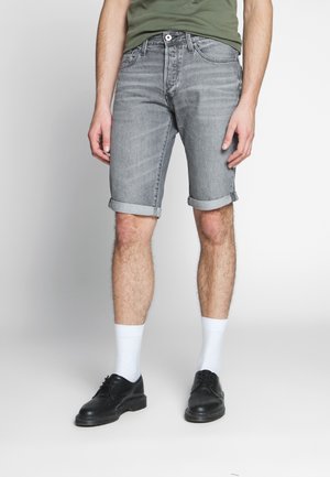 Graue Jeansshorts mit umgeschlagenen Bündchen, einem klassischen Fünf-Taschen-Design und dezentem Ausbleichen, kombiniert mit weißen Socken und schwarzen Schuhen.