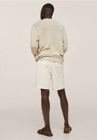 Beiger Strickpullover, weiße Shorts und braune Sandalen, getragen von einer Person, die von hinten gesehen wird. Glatte Textur und entspannte Passform.