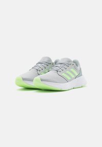 Baskets de sport grises avec une tige en mesh respirant, trois rayures vert clair et une semelle en caoutchouc texturée verte. Design moderne, construction légère.