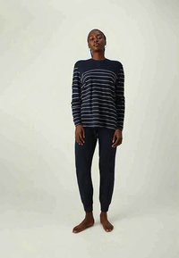 Kvinna som står barfota och bär en marinblå långärmad tröja med vita horisontella ränder och matchande marinblå joggerbyxor.