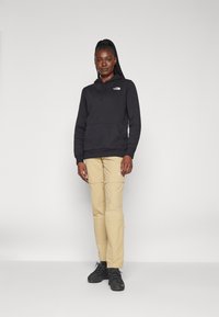 Black hooded sweatshirt with front pocket, beige zippered cargo pants, and black hiking shoes. Minimalist design, logo on the sweatshirt.