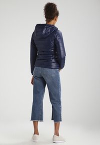 Granatowa pikowana kurtka z kapturem. W zestawie z krótkimi dżinsami i białymi butami, widziana z tyłu.