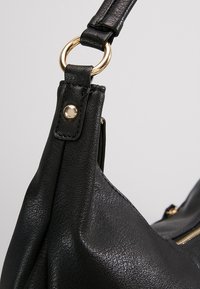 Svart syntetiskt läderhandväska med en texturerad yta, guldhardware och en böjd axelrem.