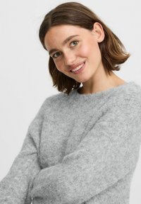 Pull en tricot gris clair, flou, avec des manches longues et un col rond, mettant en avant une texture douce et une coupe décontractée.