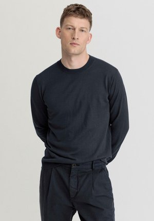 Navyblaues Langarmshirt aus weichem Stoff mit Rundhalsausschnitt und schlichter Designs, kombiniert mit dunklen Hosen, vor einem neutralen Hintergrund.