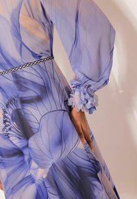 Letvægtskjole med blomsterprint i blå nuancer. Har lange ærmer, opsamlede ærmekanter med blomsterdetaljer og en sort taljebånd.