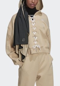 Hoodie beige corto con lacci frontali, occhielli bianchi e cordino. Abbinato a una sciarpa nera testurizzata con bordo arricciato.