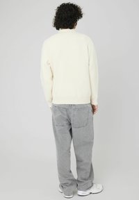 Pull crème avec des poignets et un ourlet côtelés, associé à un jean baggy gris clair avec deux poches arrière, et des baskets blanches.