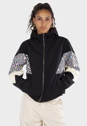 Schwarze Jacke mit Kapuze, die Ärmel mit Schachbrettmuster in Weiß, Schwarz und farblichen Akzenten aufweist. Mit Reißverschluss vorne und elastischem Saum.