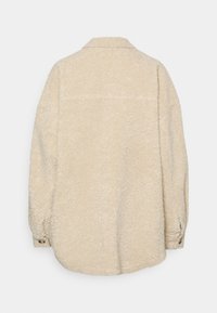 Beige Fleece-Jacke mit Kragen und langen Ärmeln. Strukturierter Stoff mit weicher Oberfläche. Knopfdetail an den Ärmeln. Nur Ansicht von hinten, keine Front sichtbar.
