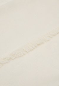 Tkanina w kolorze kremowym z subtelnym wzorem teksturowym, z frędzlami na krawędziach dla miękkiego wykończenia. Gładka powierzchnia, lekki materiał.