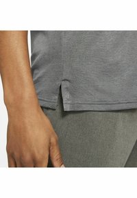 Grå sporttröja med korta ärmar, med en texturerad tyg och sidslitsar nära fållen, matchad med grå träningsbyxor.