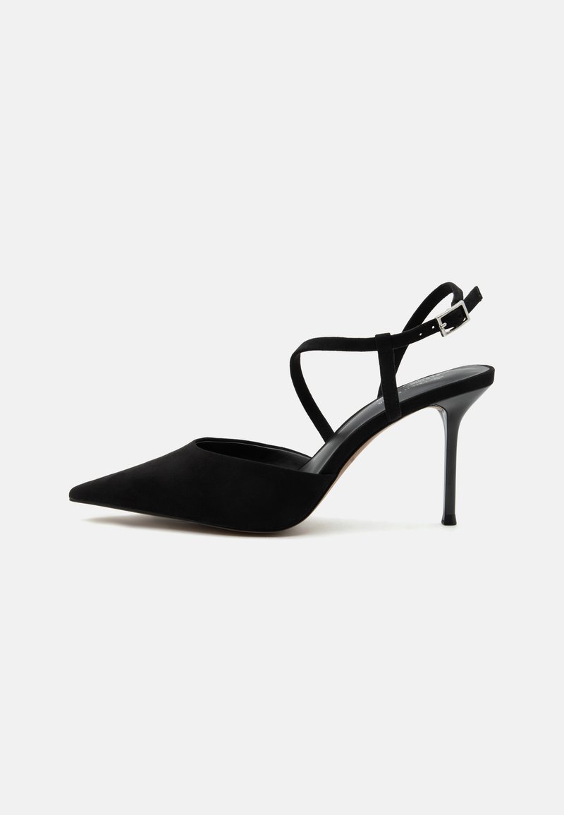 Chaussure à talon haut noire à bout pointu avec talon stiletto fin et fines lanières à la cheville avec boucle argentée sur fond blanc.