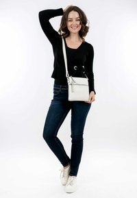 Vit crossbody-väska med en dragkedjeficka, slät textur och justerbar rem. Bärs tillsammans med en svart långärmad topp och mörkblå jeans.
