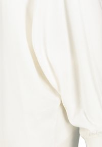 Witte katoenen trui met volumineuze mouwen en geribde manchetten. De stof heeft een gladde textuur met subtiele stikseldetails.