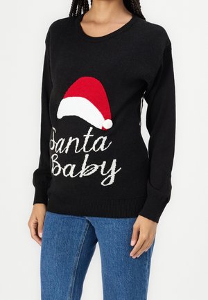 Czarny sweter z grafiką czerwono-białej czapki Mikołaja i napisem „Santa Baby”, noszony z niebieskimi dżinsami przez osobę z warkoczami.