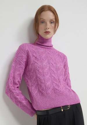 Rosa Rollkragensweater mit Zopfmuster, strukturiertem Finish und geripptem Saum sowie Bündchen, kombiniert mit schwarzen hochtaillierten Hosen.