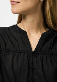 Svart blus med V-ringning och rynkade detaljer. Har knappelement längs framsidan och texturerad tyg.