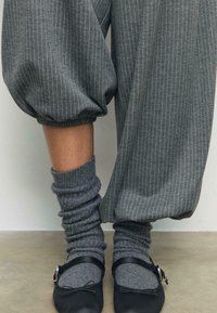 Sive hlače s prugastim uzorkom i širokim nogavicama, uparene s opuštenim sivim čarapama i crnim ravnim cipelama s detaljem kopče.