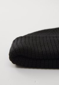 Schwarzer Strickstoff, ordentlich auf einer schlichten weißen Oberfläche gefaltet, zeigt Struktur und Rippmuster.
